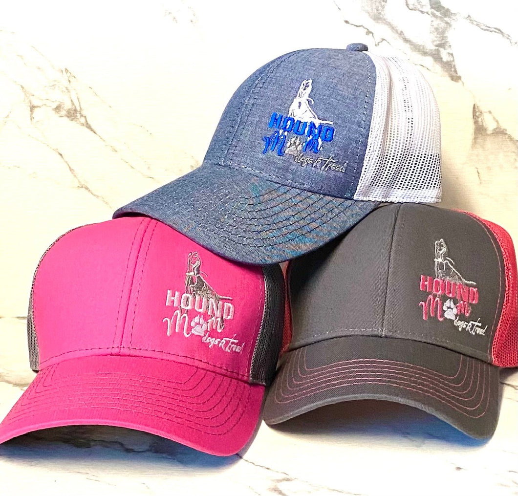 Photo is of 3 trucker style hats, in colors of pink, denim and gray stacked and facing camera. The words on left front are "Hound Mom" with the dogsRtreed logo underneath. Hats are mesh back and snap back. 