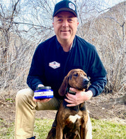 Man and dog posing in grass while man holds jar of paws R protected dog paw balm. Man in blue shirt with brown dog. Explains how to use pawsRprotected to protect your dog or animals paws or skin or heal skin irritations or minor wounds. 